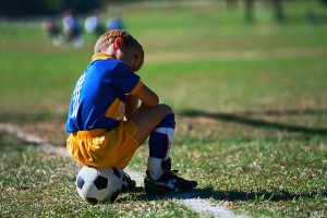 boy sits on soccer ball on sideline