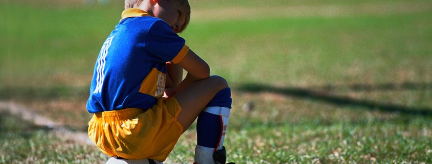 boy sits on soccer ball on sideline