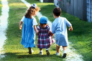 three small children holding hands and walking outside
