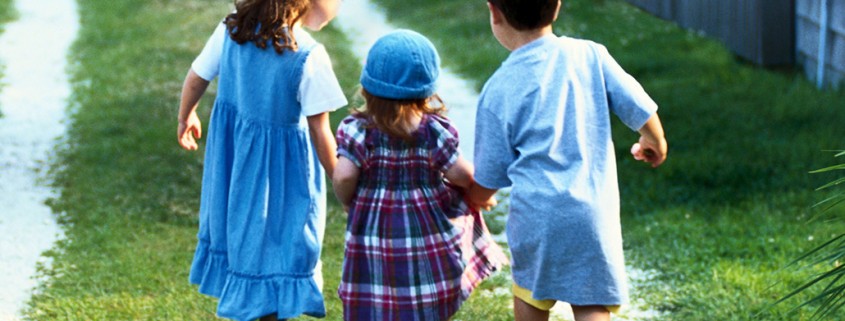 three small children holding hands and walking outside