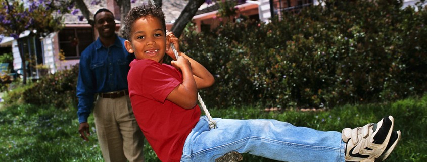 boy rides on rope swing while father looks on