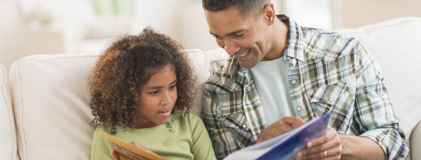 Father with daughter (6-7) reading book on sofa