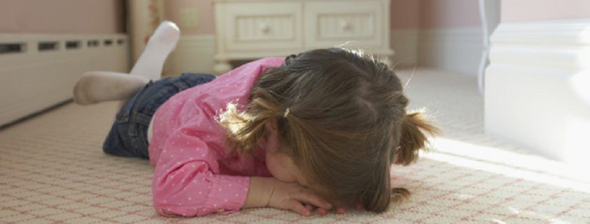 Young girl laying on bedroom carpet covering face