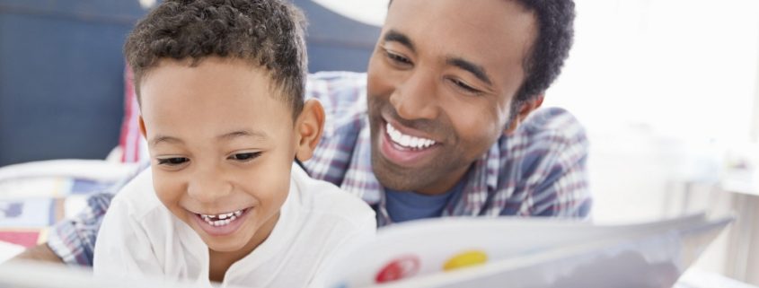 Happy father and son reading book together in bed