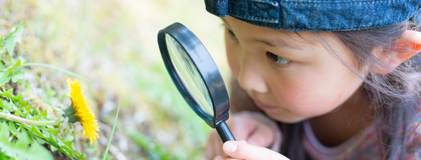 Girl with magnifying glass looking at a flower