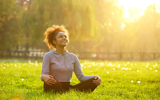 Happy young woman sitting outdoors in yoga position